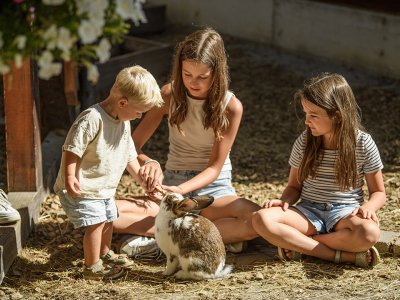 Drei Kinder sitzen und stehen auf Stroh, ein Kind füttert ein Kaninchen im Freien