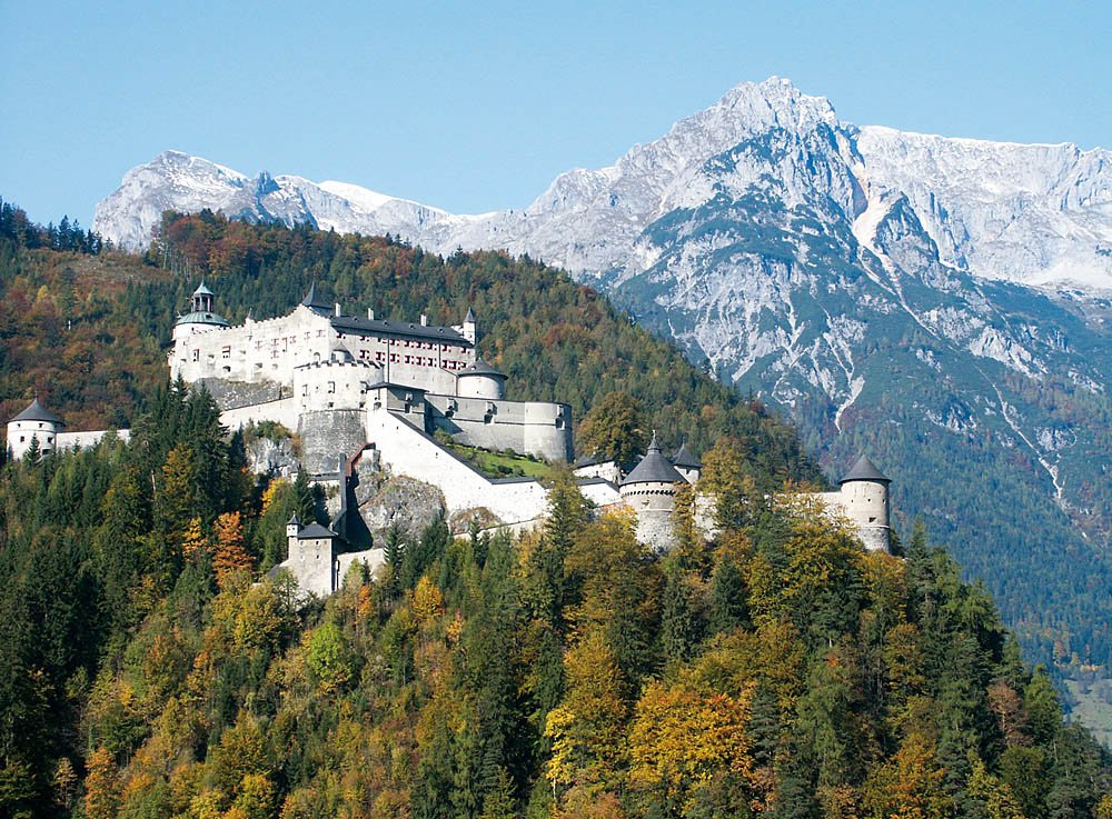 Burg Hohenwerfen umgeben von Wald mit Bergen im Hintergrund.