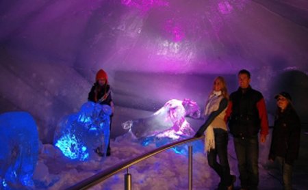 Besucher in einer beleuchteten Eishöhle mit bunten Lichteffekten.