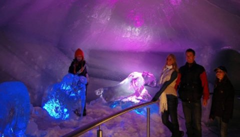 Besucher in einer beleuchteten Eishöhle mit bunten Lichteffekten.