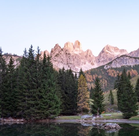 Berglandschaft mit Nadelwald und kleinem See im Sonnenuntergang.