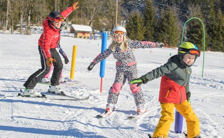 Skilehrer und Kinder üben Gleichgewicht auf sonniger Piste.