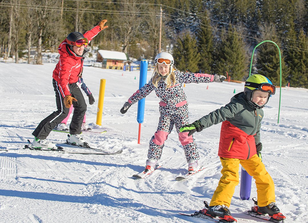 Skilehrer und Kinder üben Gleichgewicht auf sonniger Piste.