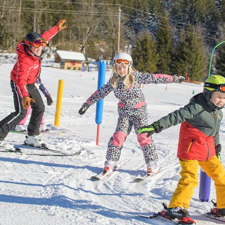 Skilehrer und Kinder üben Gleichgewicht auf sonniger Piste.