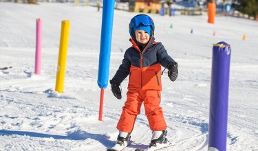 Lachender Junge fährt durch bunte Stangen im Sonnenschein.