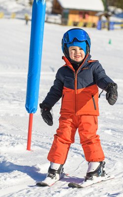 Lachender Junge fährt durch bunte Stangen im Sonnenschein.