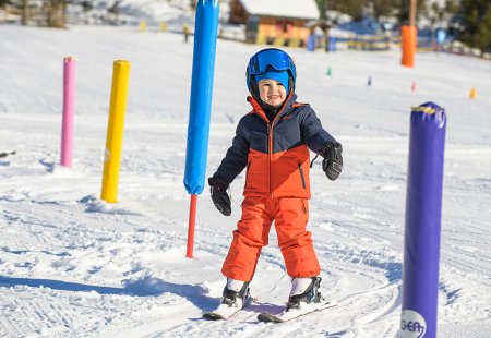 Lachender Junge fährt durch bunte Stangen im Sonnenschein.