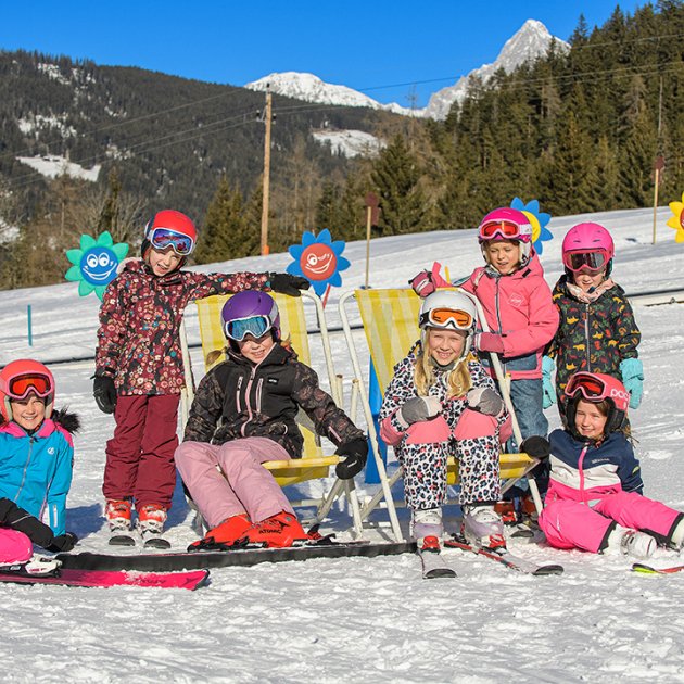 Kinder in bunten Skianzügen genießen einen sonnigen Tag auf der Piste.