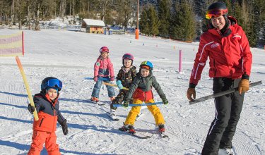 Skilehrer führt Kinder mit Stangen über verschneite Piste.