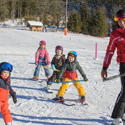 Skilehrer führt Kinder mit Stangen über verschneite Piste.