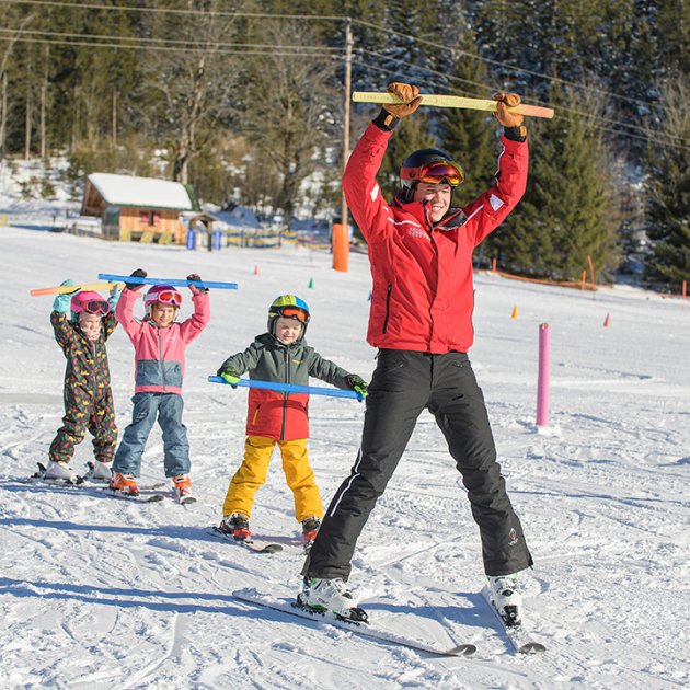 Skilehrer und Kinder heben Stangen beim Skifahren in Reihe.