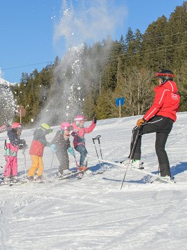 Kinder werfen Schnee hoch bei lustiger Skistunde.