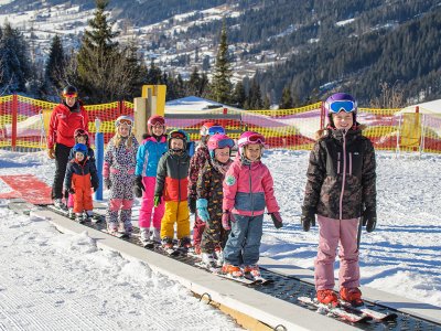 Kindergruppe mit Skilehrer auf Förderband im Schnee.