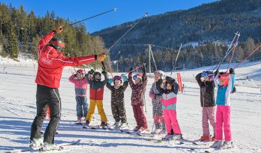 Skilehrer und Kinder heben Skistöcke während der Skistunde.