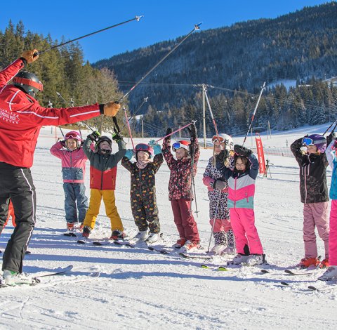 Skilehrer und Kinder heben Skistöcke während der Skistunde.
