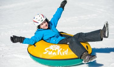 Lachendes Kind rutscht im gelben Reifen über den Schnee.