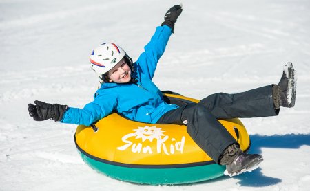 Lachendes Kind rutscht im gelben Reifen über den Schnee.