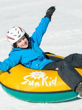 Lachendes Kind rutscht im gelben Reifen über den Schnee.