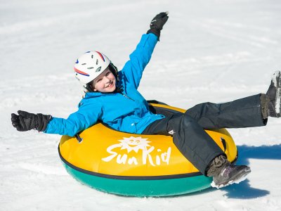 Lachendes Kind rutscht im gelben Reifen über den Schnee.