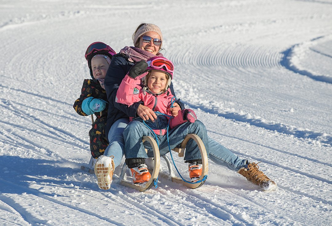 Lachende Frau rodelt mit zwei fröhlichen Kindern im Schnee.