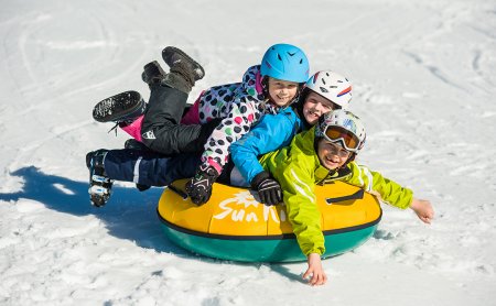 Drei fröhliche Kinder liegen auf einem Schneereifen übereinander.