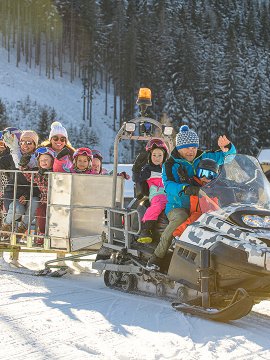 Schneemobilfahrt mit fröhlich winkenden Kindern und Erwachsenen im Winterpanorama.
