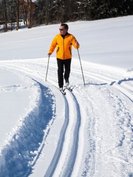 Männer und Frauen beim Langlaufen auf verschneiten Loipen in einer winterlichen Landschaft.
