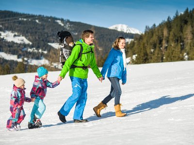 Familienwanderung über verschneiten Hang mit Bergblick.