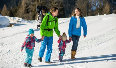 Familie mit Kindern wandert durch verschneite Winterlandschaft.