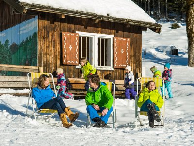 Erwachsene entspannen im Liegestuhl, Kinder spielen im Schnee.