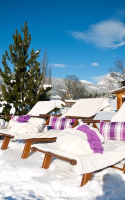 Gemütliche Liegestühle mit Decken in verschneiter Alpenlandschaft.
