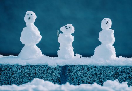 Drei kleine Schneemänner auf einer verschneiten Mauer.