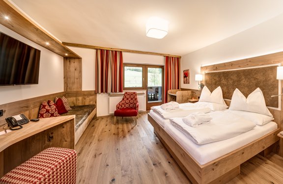 Helles Doppelzimmer mit Holzmöbeln, gemütlicher Sitzecke und Balkonblick.