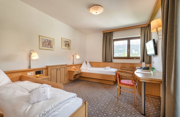 Helles Zweibettzimmer mit Holzmöbeln, Schreibtisch und Fenster mit Bergblick.