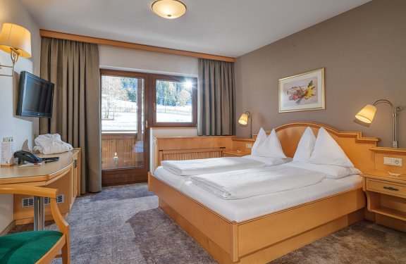 Gemütliches Doppelzimmer mit Balkon, Schreibtisch und Blick auf Wiese und Wald.