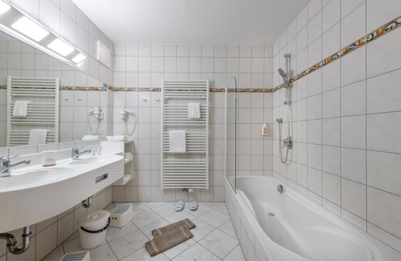 Helles Bad mit Badewanne, Doppelwaschbecken und Handtuchheizkörpern.
