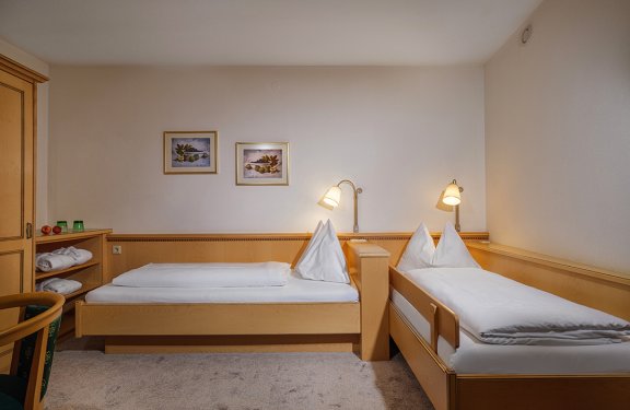 Helles Zweibettzimmer mit zwei Einzelbetten, Holzmöbeln und sanfter Beleuchtung.