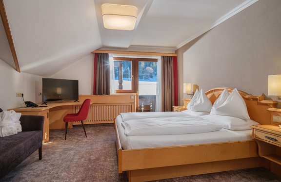 Helles Doppelzimmer mit Dachschräge, Schreibtisch, Sofa und Balkonzugang.