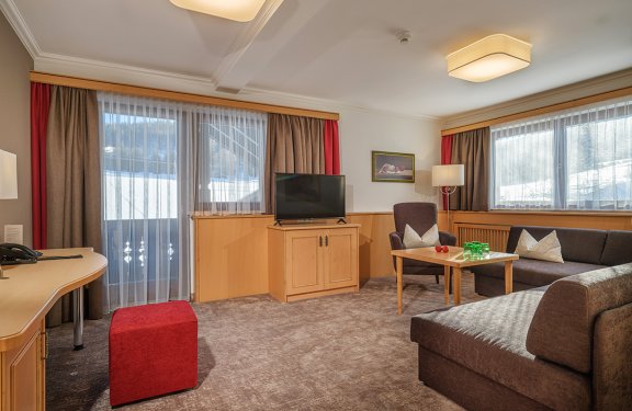 Großer Wohnbereich mit Sofa, Sessel, TV und großen Fenstern mit Bergblick.