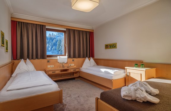 Gemütliches Zimmer mit zwei Einzelbetten, warmen Holzmöbeln und Blick in den Winterwald.