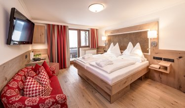 Modernes Doppelzimmer mit Holzmöbeln, rotem Sofa und Zugang zum eigenen Balkon.