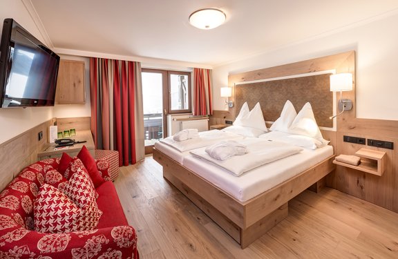 Modernes Doppelzimmer mit Holzmöbeln, rotem Sofa und Zugang zum eigenen Balkon.