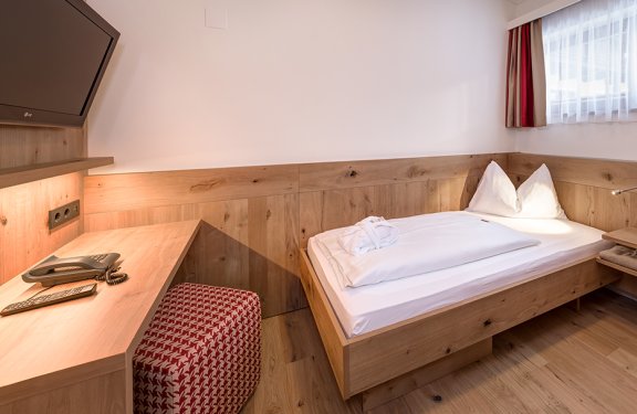 Modernes Einzelzimmer mit Holzmöbeln, Schreibtisch und großem Fenster.