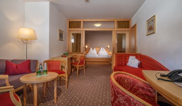 Großzügige Suite mit Wohnbereich, Doppelbett und Glasabtrennung für Privatsphäre.