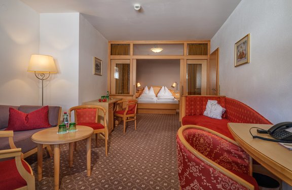 Großzügige Suite mit Wohnbereich, Doppelbett und Glasabtrennung für Privatsphäre.