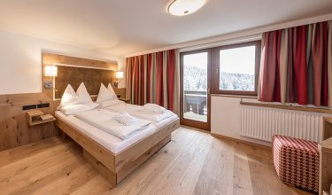 Modernes Doppelzimmer mit Holzmöbeln, Balkon und Blick auf verschneiten Wald.