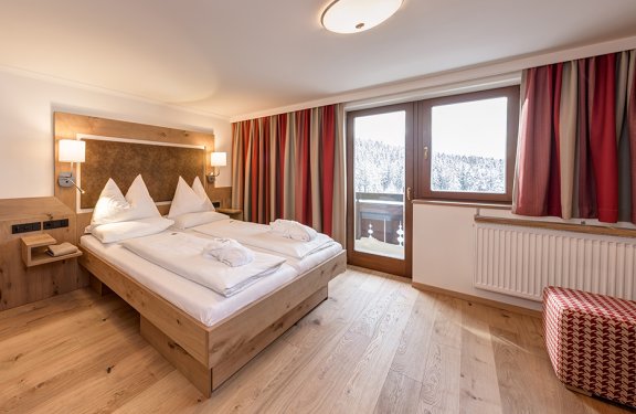 Modernes Doppelzimmer mit Holzmöbeln, Balkon und Blick auf verschneiten Wald.