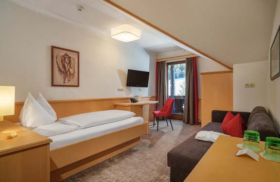 Gemütliches Einzelzimmer mit Dachschräge, Sofa, Schreibtisch und Balkonzugang.