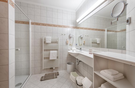 Helles Bad mit begehbarer Dusche, großem Spiegel und Handtuchheizkörpern.