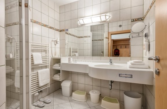 Helles Bad mit Doppelwaschbecken, Dusche, Handtuchheizung und Kindertritthockern.